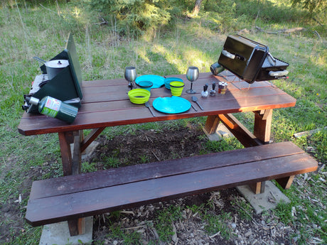 Outdoor dining setup on a picnic table: a camp stove, grill, & colorful dishes. Perfect for your RV rental getaway!