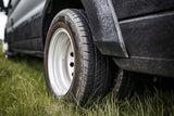 Close-up of an RV rental's rear dual wheels on a textured black body, parked on green grass.