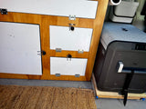 An rv rental's interior: custom wood cabinetry with white doors, a large Dometic CFX cooler, and a woven mat.