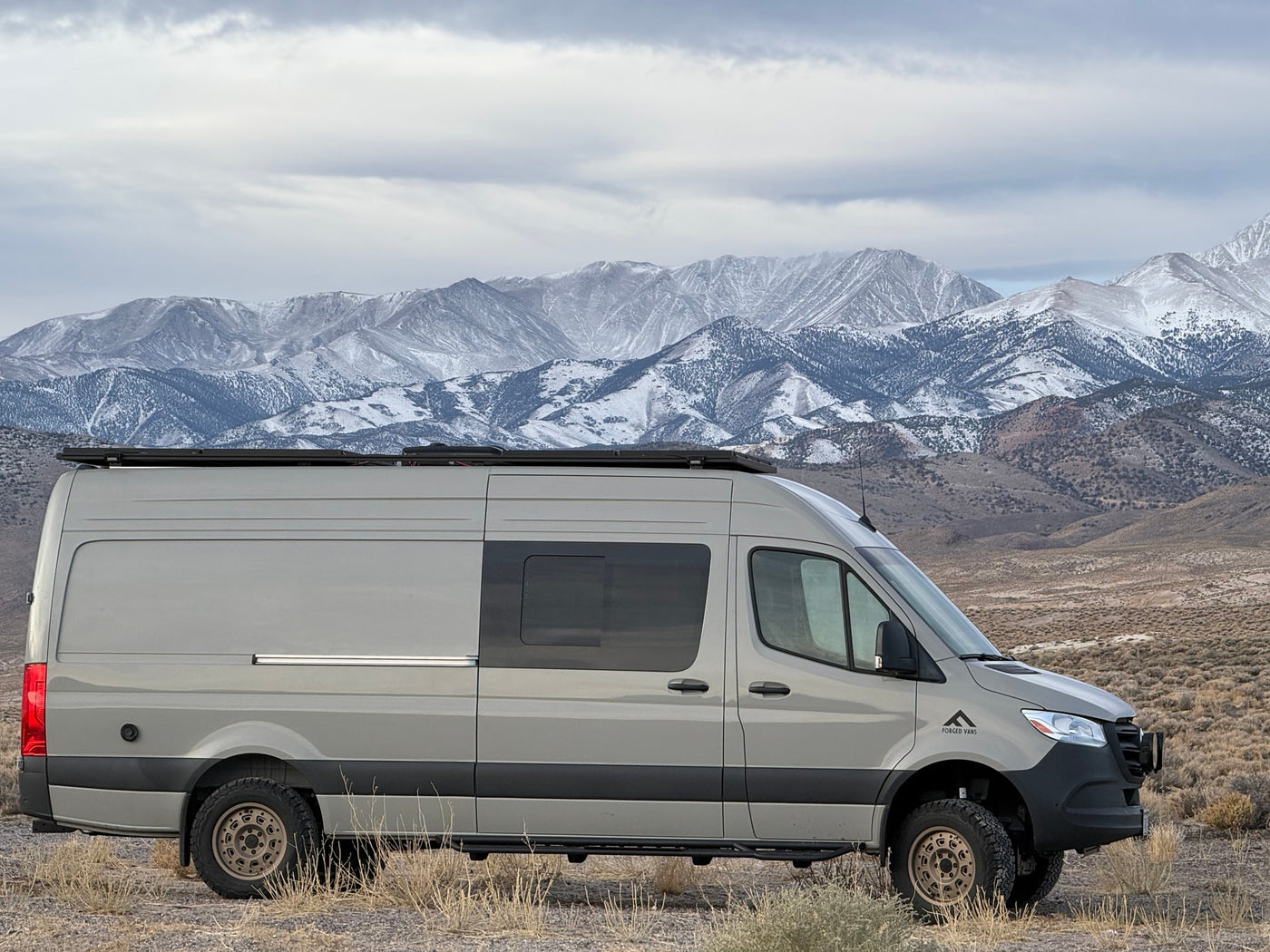 Rugged grey camper van, ideal for an RV rental, parked in a vast, dry landscape with stunning snow-capped mountains. — photo 13