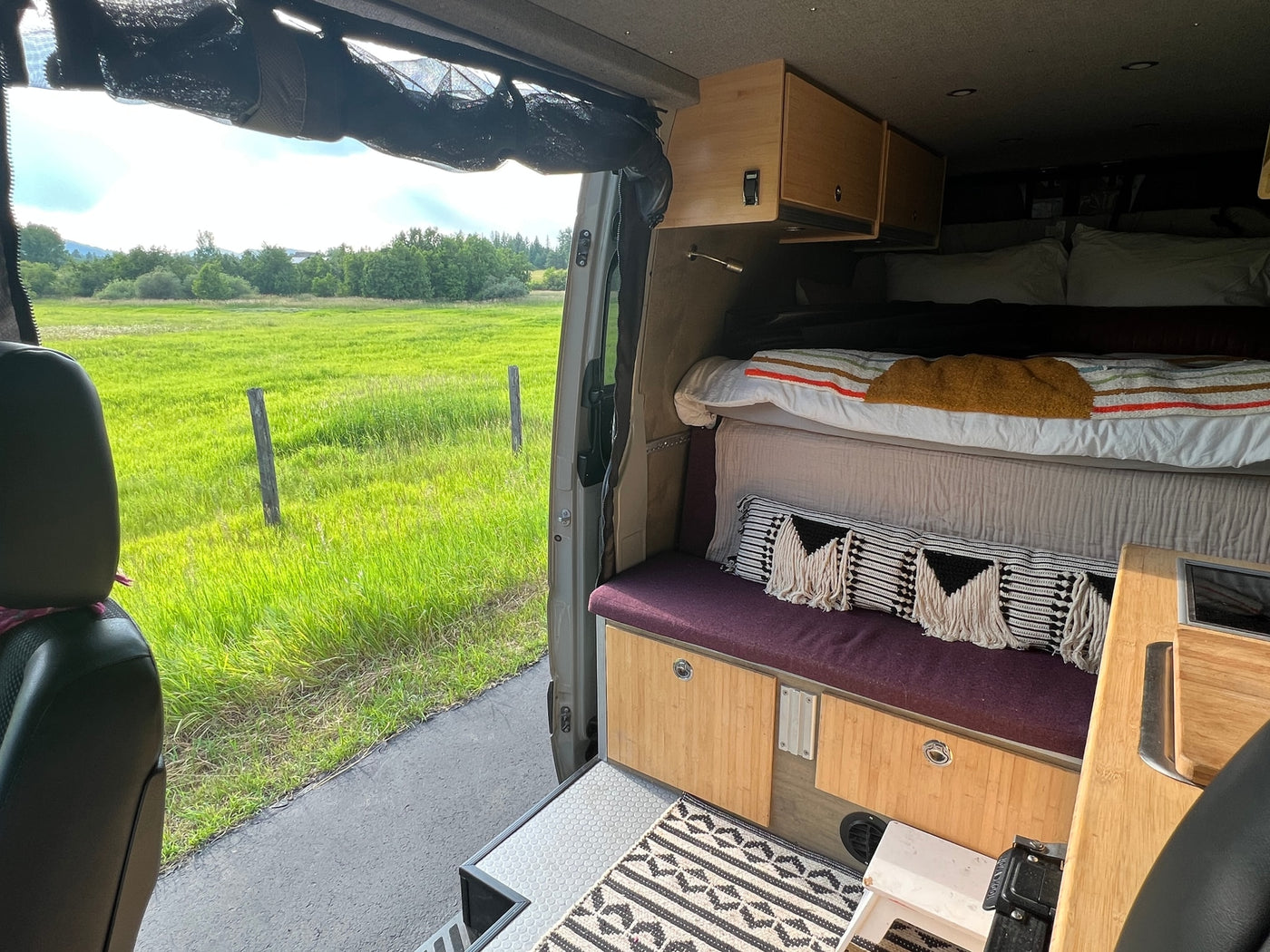 Experience van life in this RV rental: a comfy bed, custom cabinetry, and stunning views of a green field. — photo 20