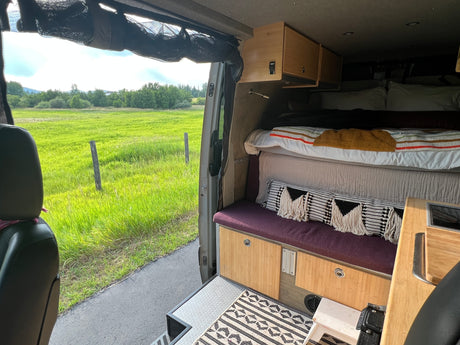 Experience van life in this RV rental: a comfy bed, custom cabinetry, and stunning views of a green field.