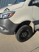 Front-side view of a white Forged Vans Sprinter camper van, equipped with Outpost A/T tires. Excellent for RV rental adventures.