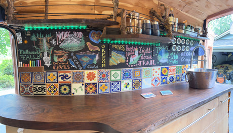 RV rental kitchen: Custom Oregon travel map drawn on chalkboard, vibrant tiled backsplash, wooden counter, and sink.