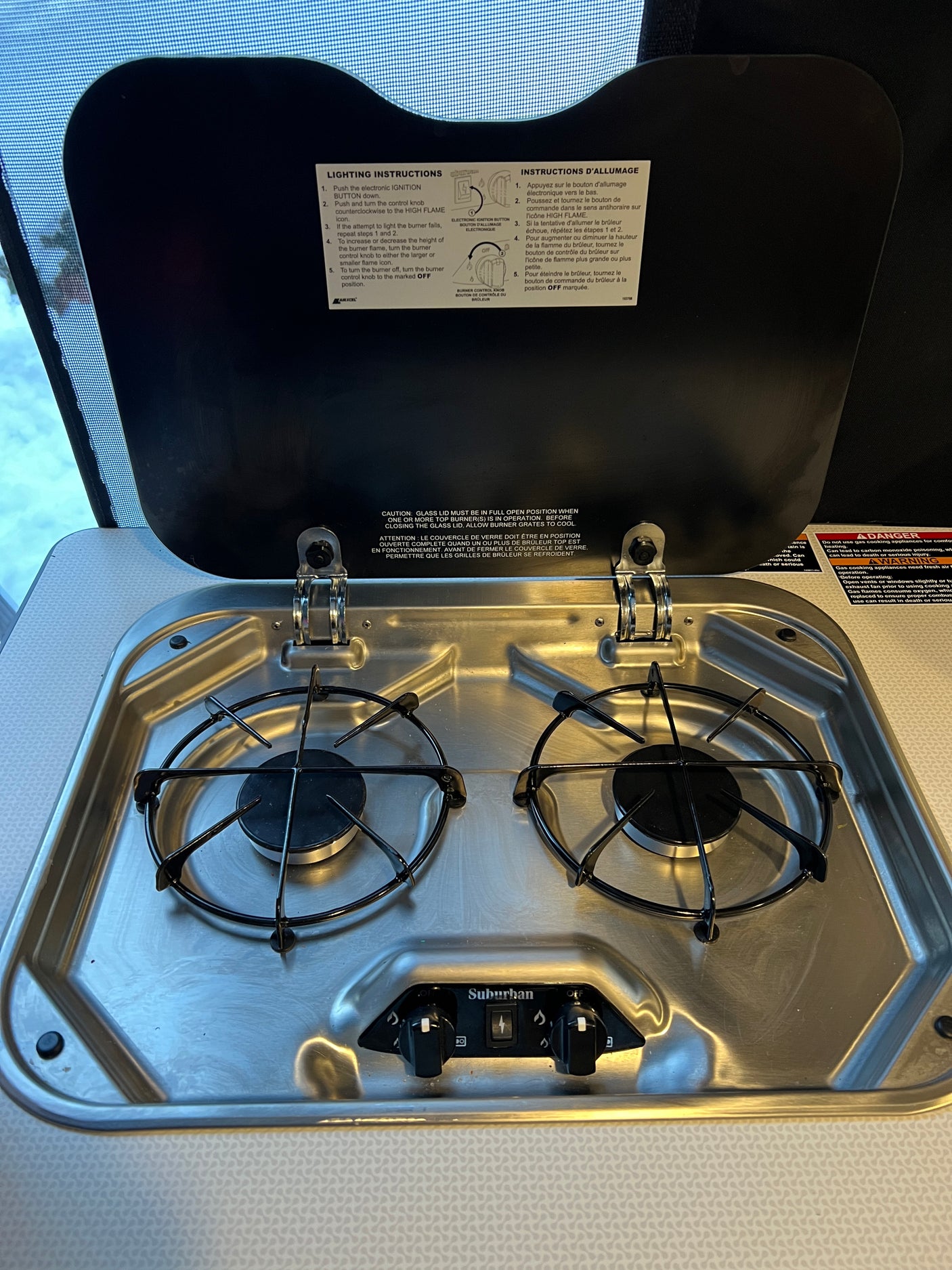 Clean two-burner stainless steel gas cooktop in an RV rental, with the lid open to reveal lighting instructions.