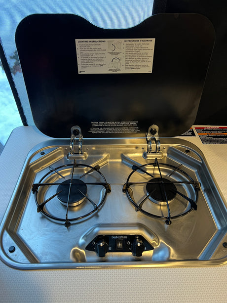 Clean two-burner stainless steel gas cooktop in an RV rental, with the lid open to reveal lighting instructions.