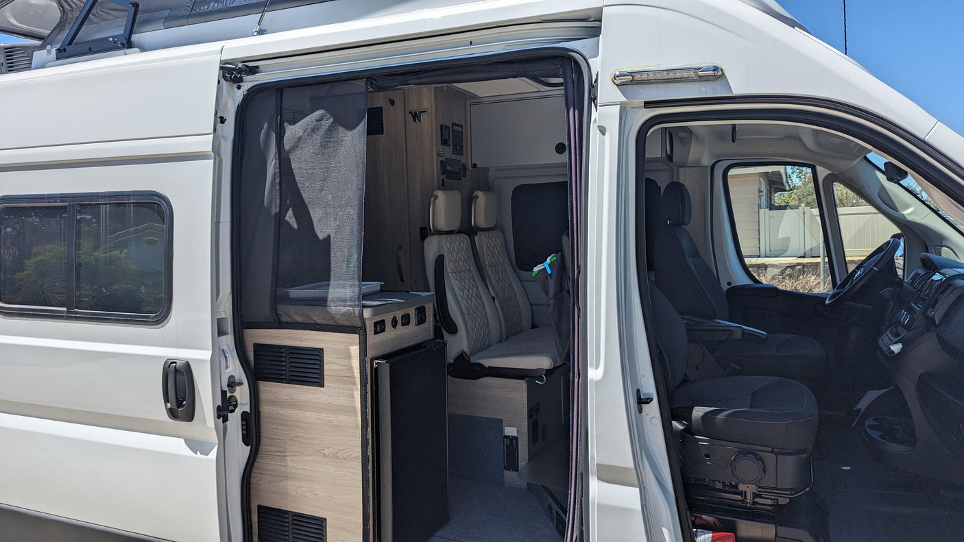 This white RV rental showcases its open side door, revealing a modern interior with a kitchen, seating, and the front cabin.