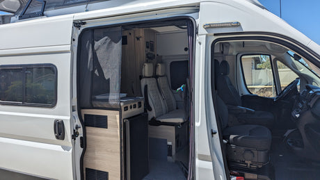 This white RV rental showcases its open side door, revealing a modern interior with a kitchen, seating, and the front cabin.