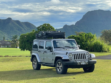 Adventure awaits! Silver Jeep with rooftop tent for your RV rental journey, set against stunning Kauai mountains.