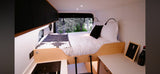 Explore in comfort with this RV rental! Features a cozy bed and compact kitchen in a modern camper van interior.