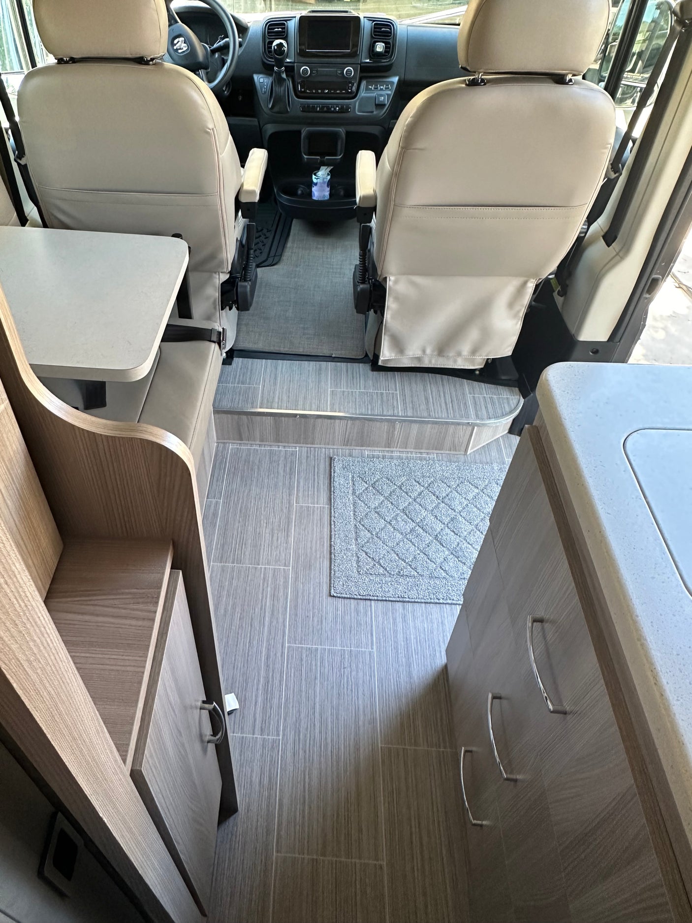Inside an RV rental: front seats, dashboard, and compact living area with kitchenette.