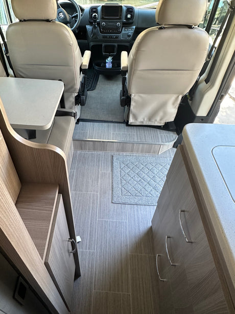 Inside an RV rental: front seats, dashboard, and compact living area with kitchenette.
