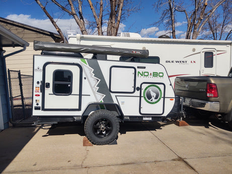 A white 'No Boundaries' travel trailer and a large 'Due West' RV, ideal for an rv rental trip, parked with a pickup truck.