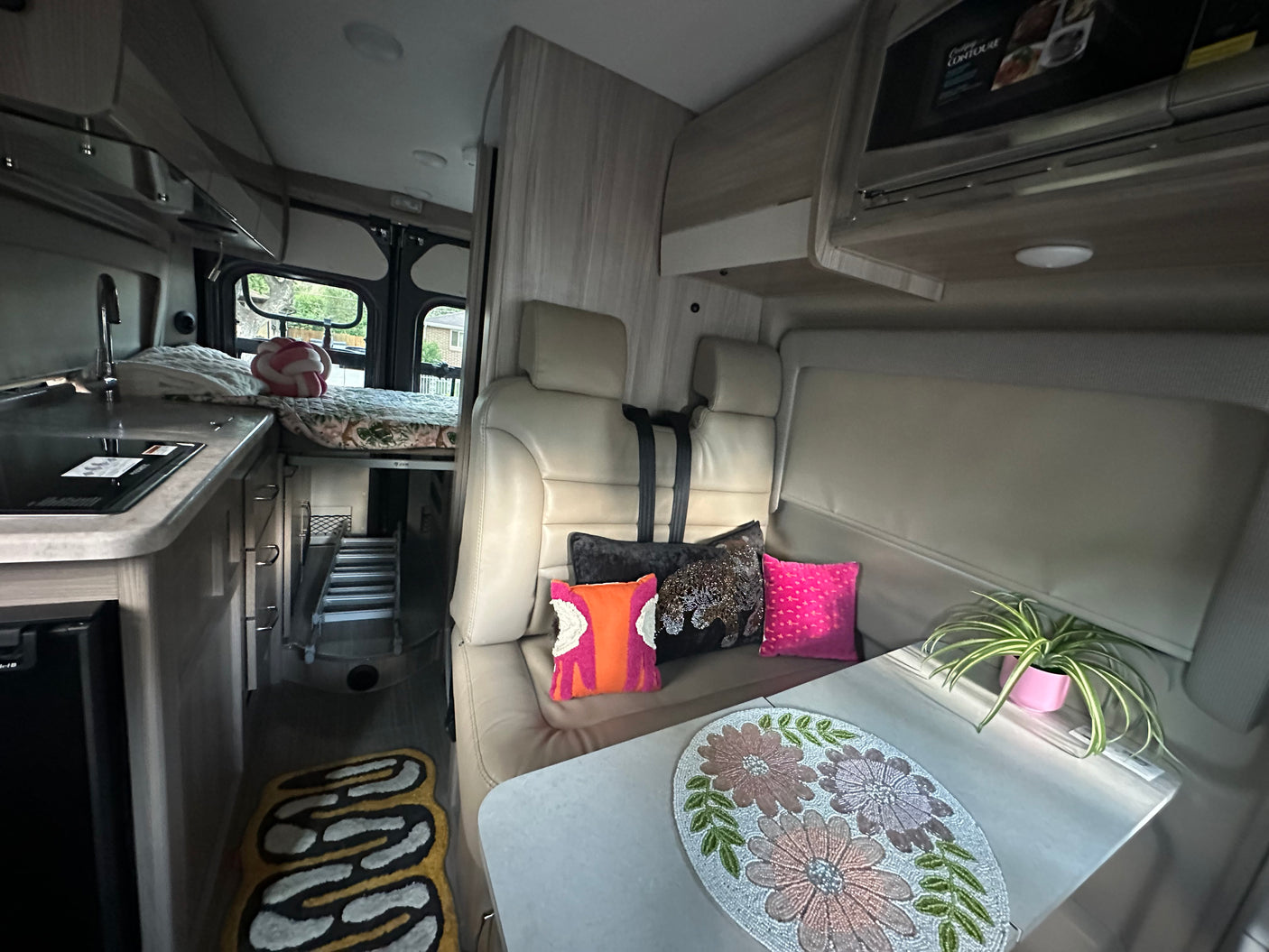 Explore this comfy RV rental interior. Features a dining area, kitchen counter, and elevated bed with small steps.