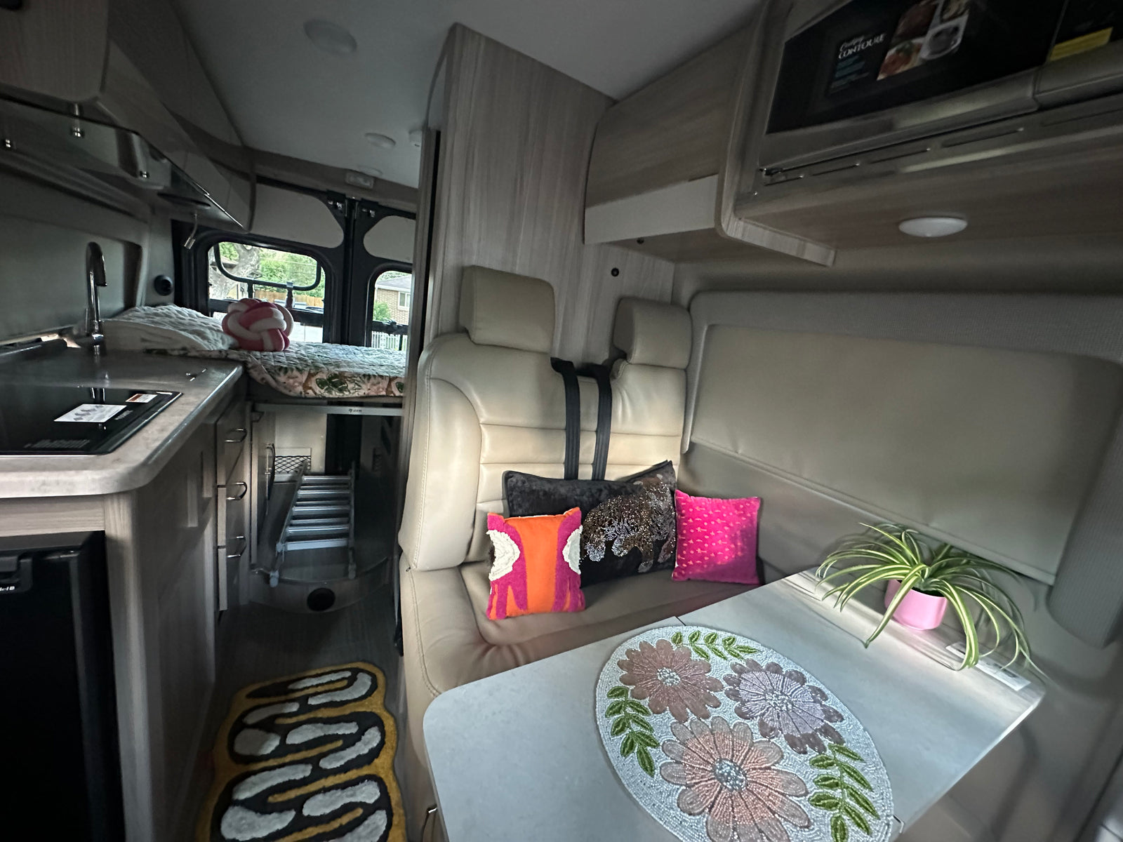 Explore this comfy RV rental interior. Features a dining area, kitchen counter, and elevated bed with small steps.