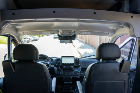 Front cabin view of an RV rental, showcasing the modern dashboard, navigation screen, and driver's area for a clear road ahead.