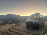 Sunrise at a mountain campsite featuring an RV rental Mercedes Sprinter camper van and a warm campfire. Perfect for outdoor adventures.