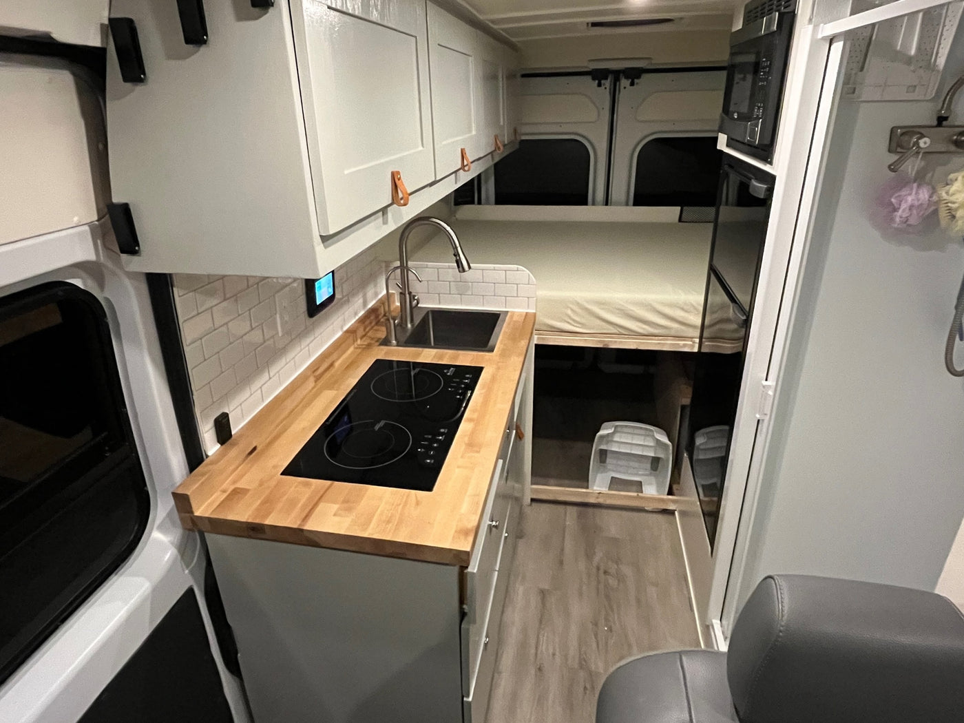 This RV rental's modern interior features a sleek kitchen with cooktop and sink, a raised bed, and smart storage. — photo 2