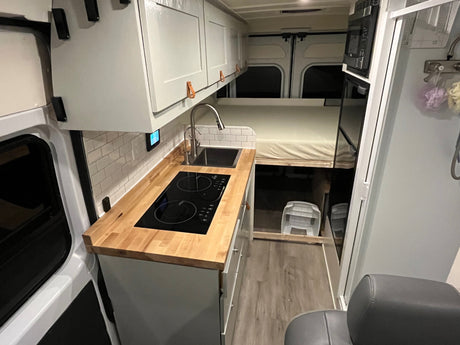 This RV rental's modern interior features a sleek kitchen with cooktop and sink, a raised bed, and smart storage.