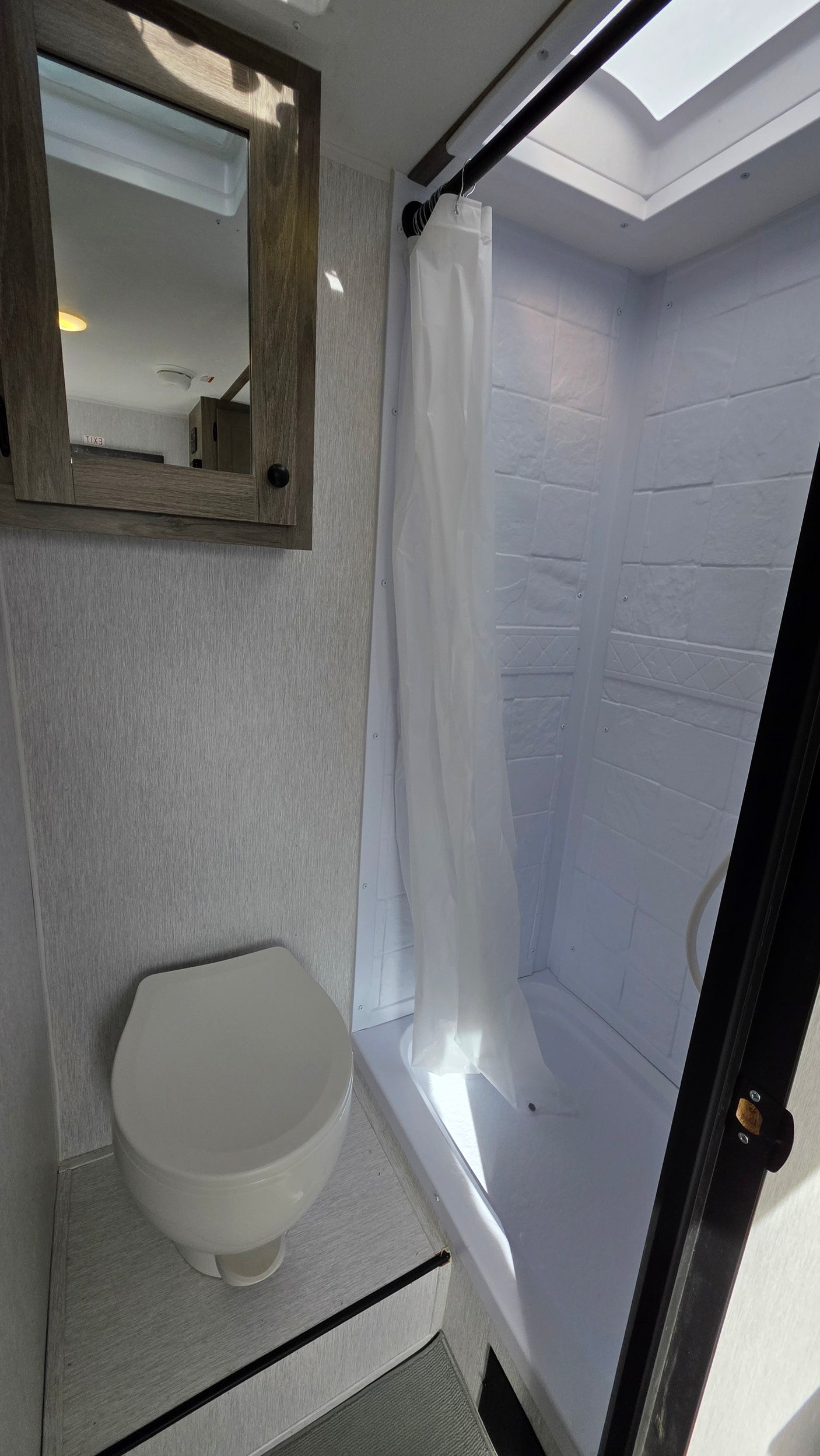 Compact RV rental bathroom: clean toilet, shower with skylight, and mirror for comfort on the road.