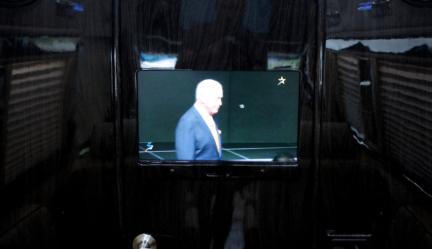 Luxury RV rental interior with an embedded TV showing a man, framed by dark wood paneling & reflections of blinds.