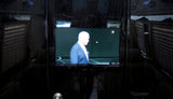 Luxury RV rental interior with an embedded TV showing a man, framed by dark wood paneling & reflections of blinds.