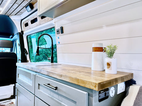 Modern RV rental kitchen in a van conversion, featuring a wooden counter, sink, and integrated controls for comfortable travel.