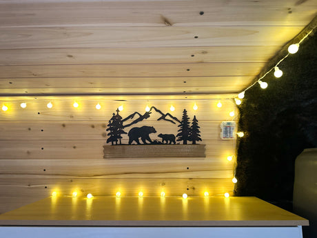 Cozy RV rental interior with warm string lights, wooden paneling, and a bear-mountain metal art piece. Great for trips!
