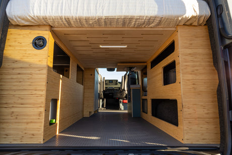 Inside a custom bamboo camper van conversion with rear bed & ample storage, ideal for an rv rental.