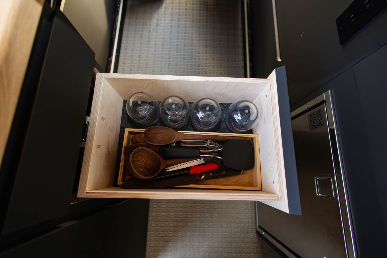 An RV rental kitchen drawer with neatly organized glasses, wooden spoons, and cooking utensils for your journey.