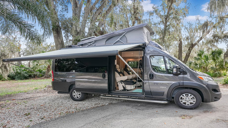 This gray Jayco Swift camper van, ideal for RV rental, is parked outdoors with its pop-top and awning extended.