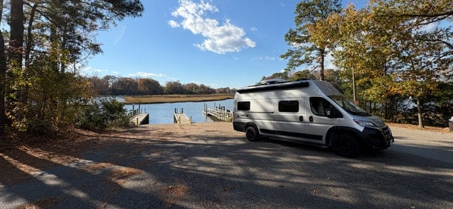 RV rental parked at a scenic waterfront boat ramp, surrounded by autumn trees under a clear blue sky. — photo 18