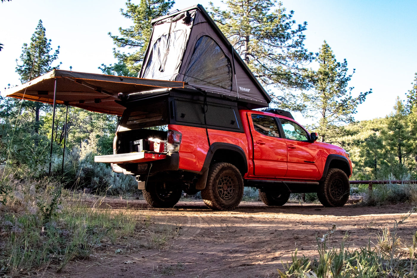  perfect for an off-road RV rental camping adventure in the forest.|Bright orange Toyota Tacoma truck with rooftop tent and awning on a dirt path; ideal for an RV rental.|An orange Toyota Tacoma overlander — photo 2