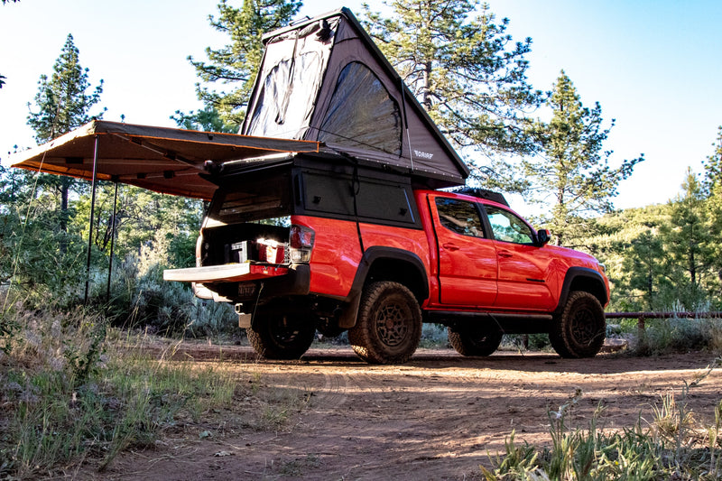  perfect for an off-road RV rental camping adventure in the forest.|Bright orange Toyota Tacoma truck with rooftop tent and awning on a dirt path; ideal for an RV rental.|An orange Toyota Tacoma overlander — photo 2