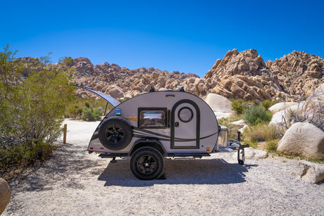 Teardrop camper RV rental parked in a rugged desert landscape with large rock formations and blue sky, ready for adventure.