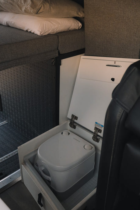 RV rental interior: bed, Dometic portable toilet stored in a pull-out compartment, and a seat for compact comfort.