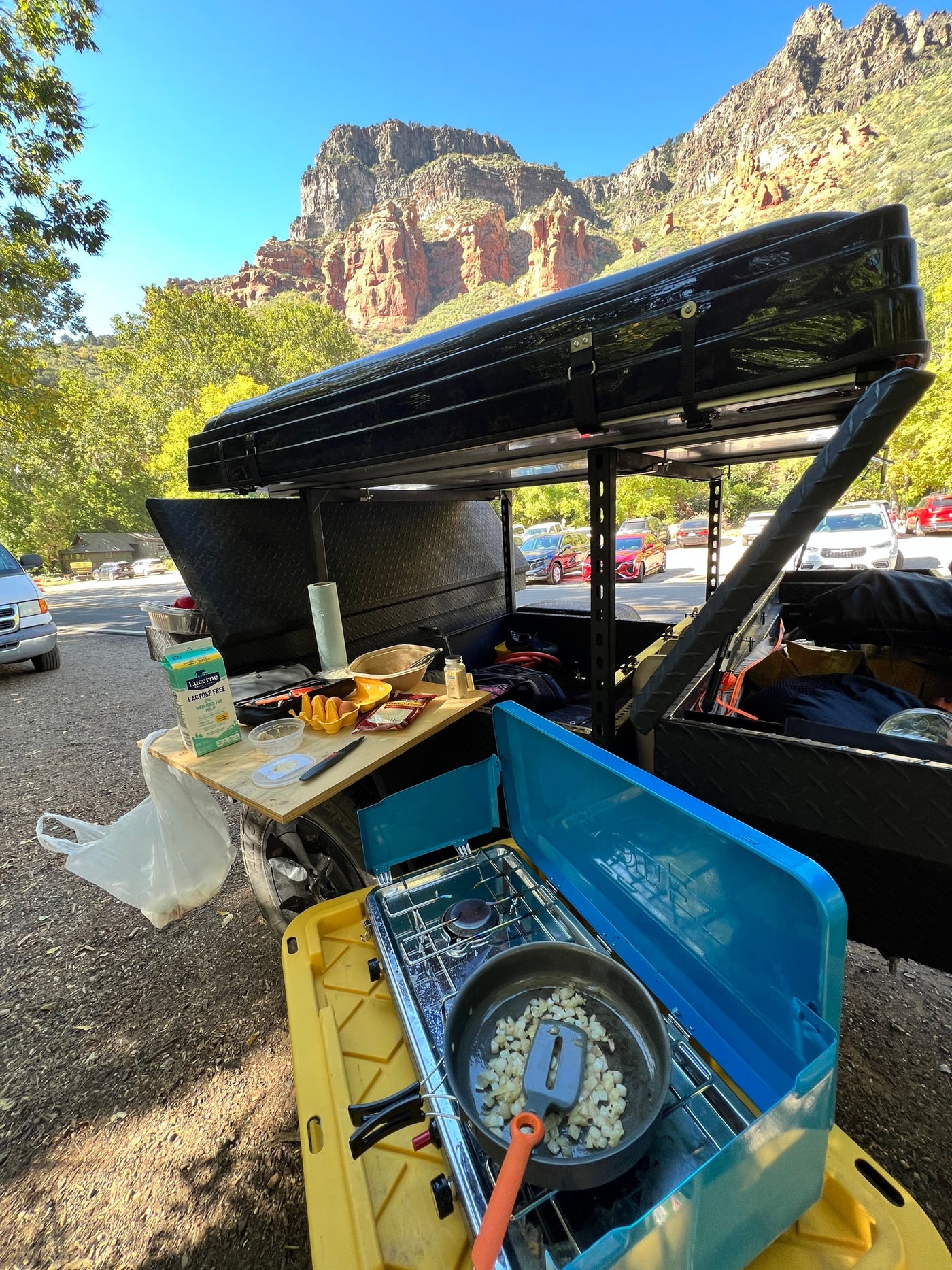 An outdoor cooking setup with a pan and food on a table, next to an overland camping trailer, at a scenic location with red rock mountains. Ideal for an rv rental trip. — photo 19