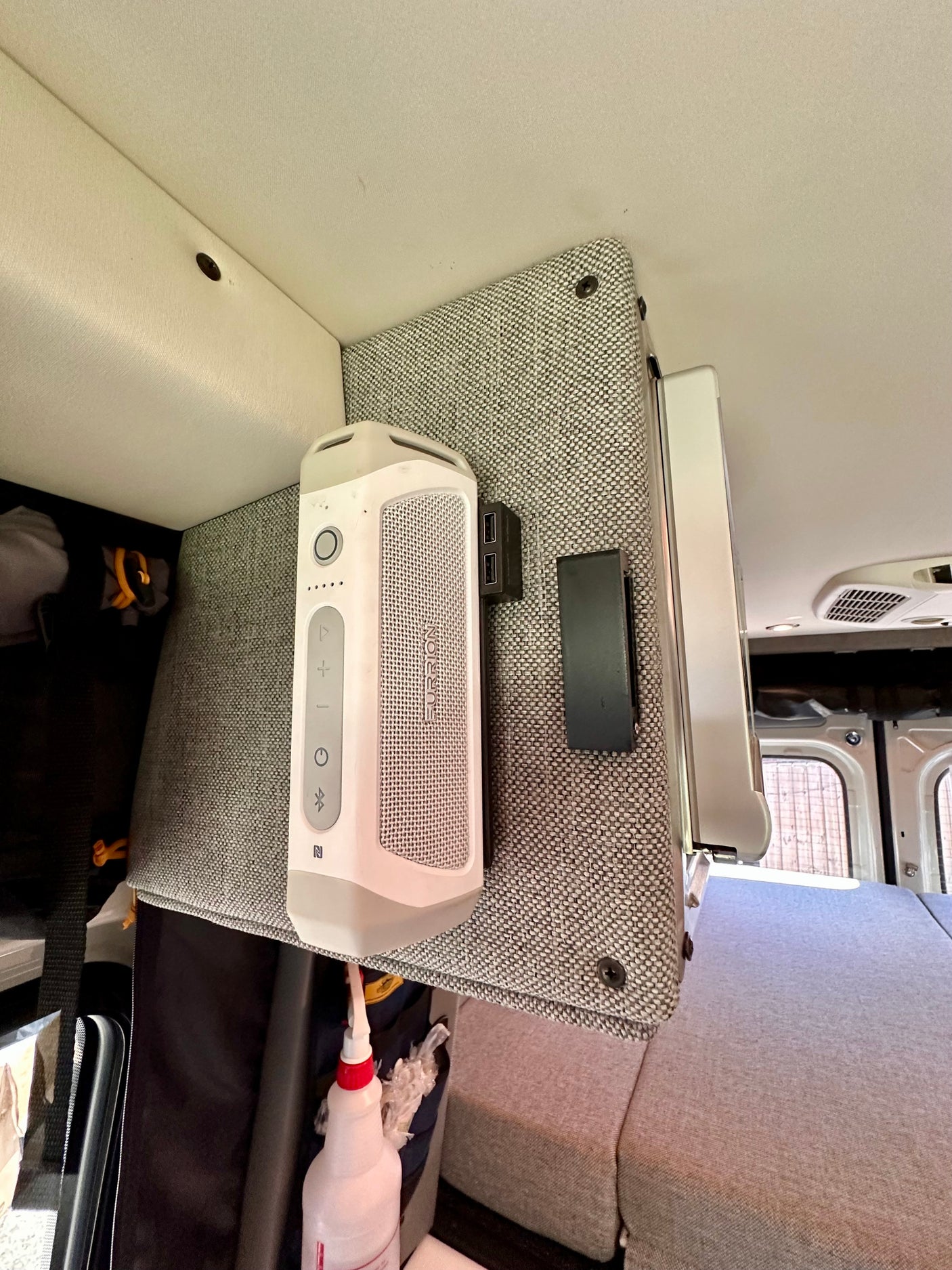 RV rental interior: A white portable speaker and USB hub mounted on a fabric panel above a grey bed.