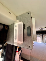 RV rental interior: A white portable speaker and USB hub mounted on a fabric panel above a grey bed.