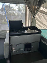 Explore this RV rental's pop-up camper interior, featuring a compact kitchen with stove, sink, & storage. Ideal for camping.