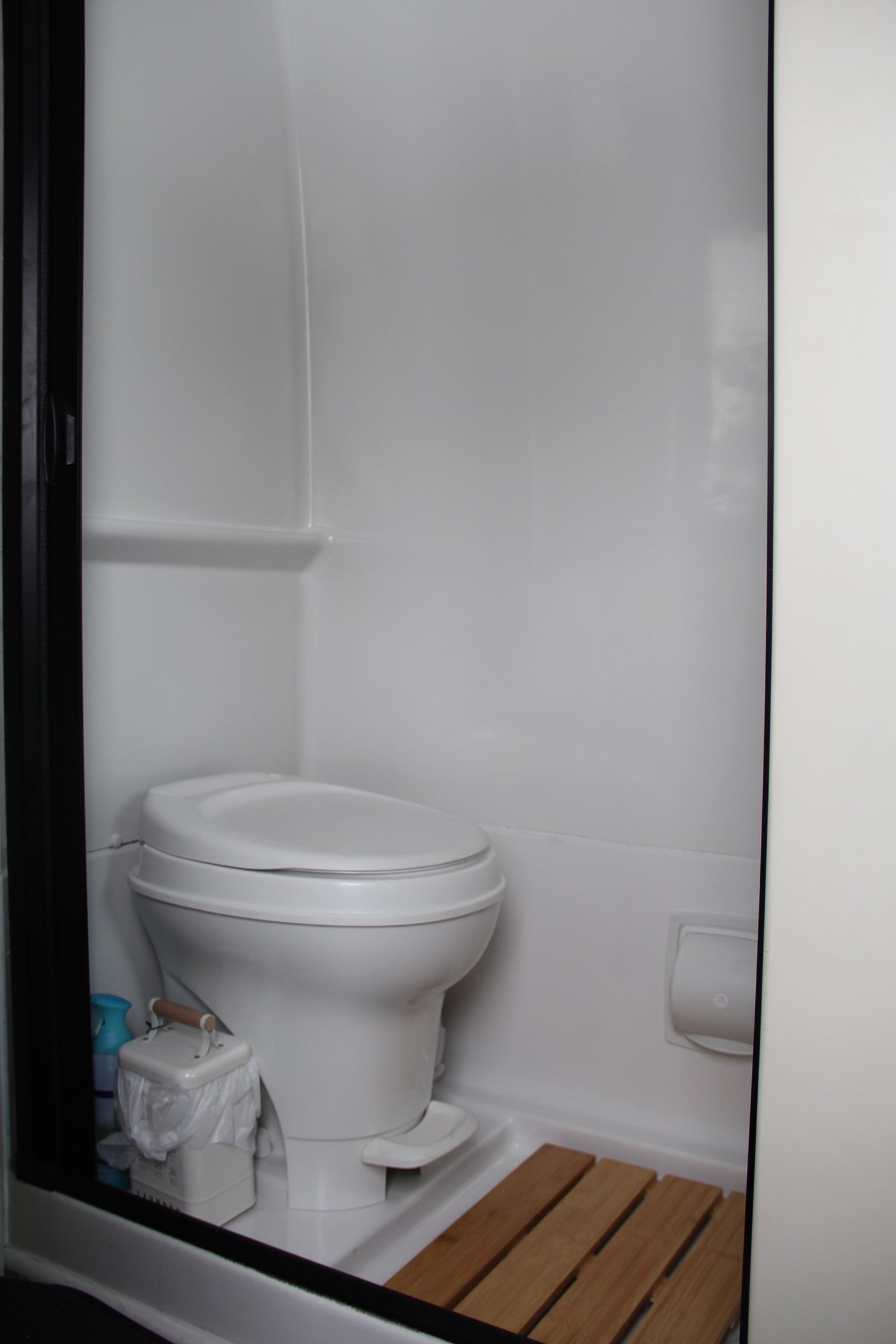 RV rental: Compact bathroom with white toilet, small bin, and slatted wooden floor.