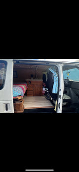 RV rental interior: A converted camper van's cozy living space with a bed, kitchenette, and wood floors.