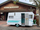 Vintage white & teal RV rental outside "Hall of Flowers". Open door reveals retro interior design.