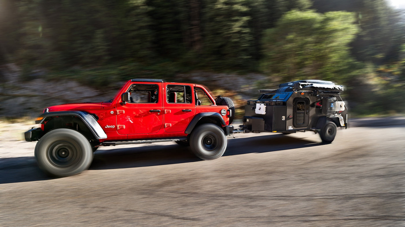 Red Jeep Gladiator towing a rugged black rv rental for off-road camping, in motion on a scenic road. — photo 5