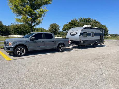 A grey truck tows a compact travel trailer on asphalt under a clear sky. Ideal for your next RV rental and camping adventure!
