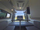 Modern RV rental interior: laptop on dinette table, perfect for remote work with scenic views of nature.