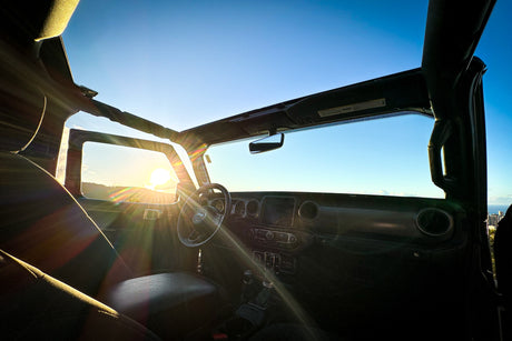 Inside a Jeep Wrangler at sunset, sun flares beam. Ready for travel, perhaps an RV rental adventure.