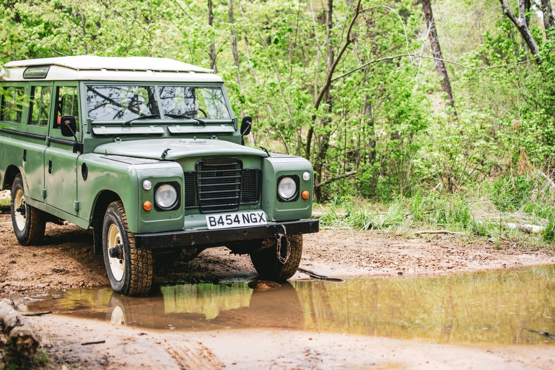 A classic green Land Rover on a muddy trail, perfect for an off-road rv rental adventure in nature.