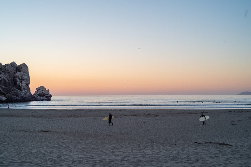 Surfers on a sandy beach with rock formations at sunset. Imagine a relaxing RV rental trip ending here. — photo 16
