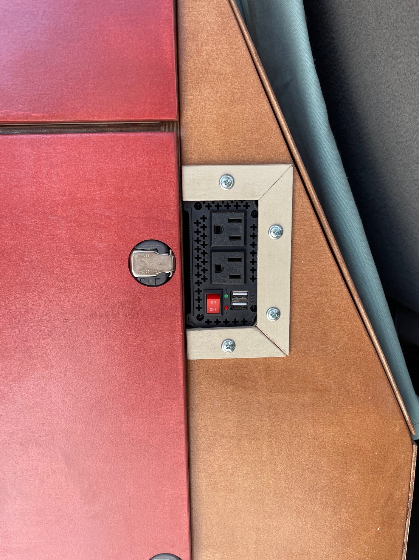 RV rental power inverter with AC outlets, USB ports, and an on/off switch, custom-built into wooden cabinetry.
